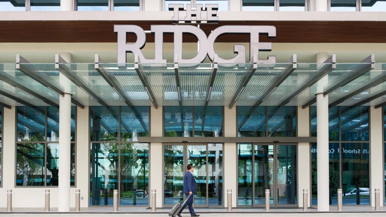 A guest wheels his luggage past the entrance of The Ridge, its name in large letters above the glass canopy